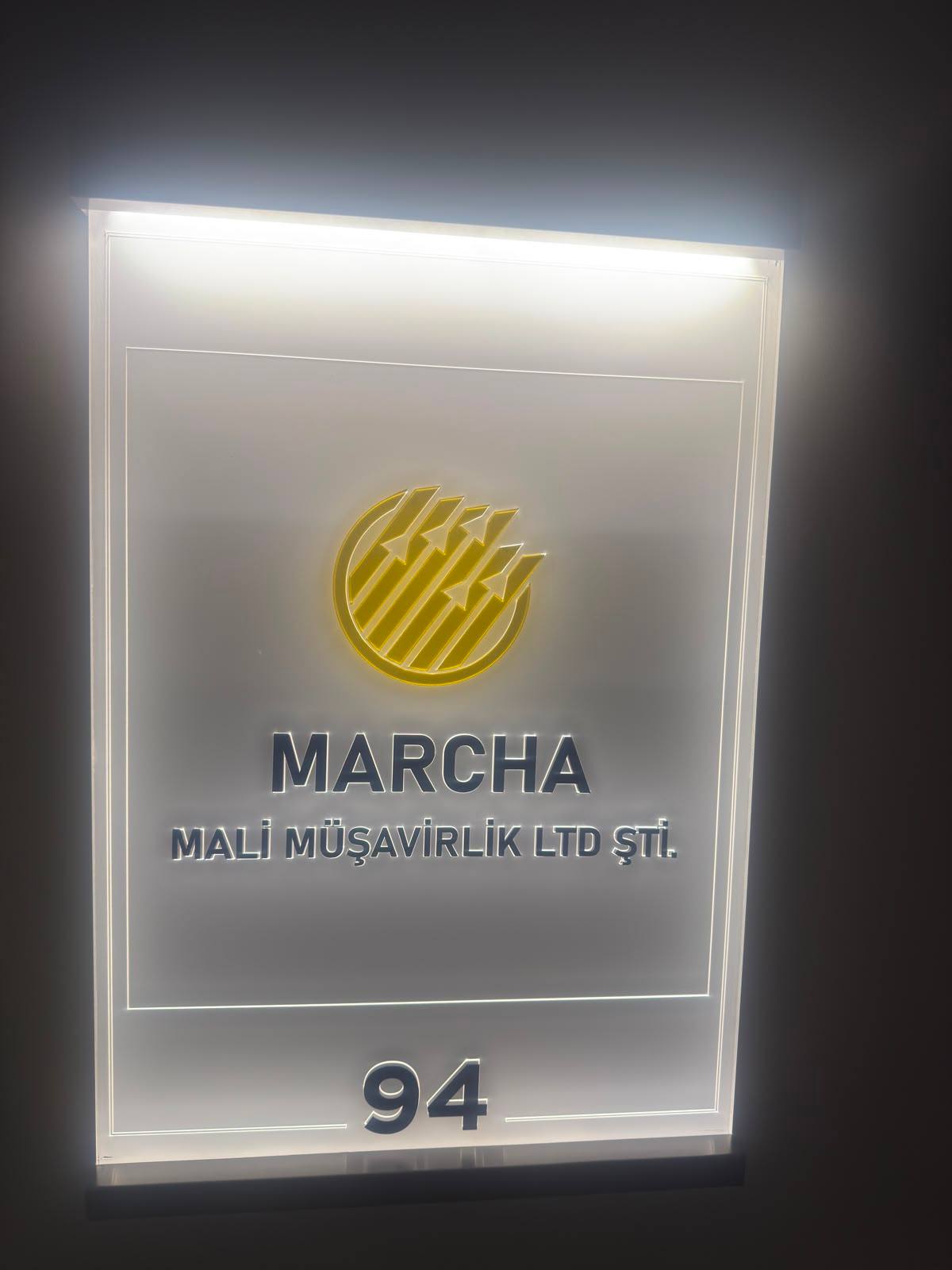 Ofis kapısındaki aydınlatmalı tabela: Marcha Mali Müşavirlik Ltd. Şti., kapı numarası 94